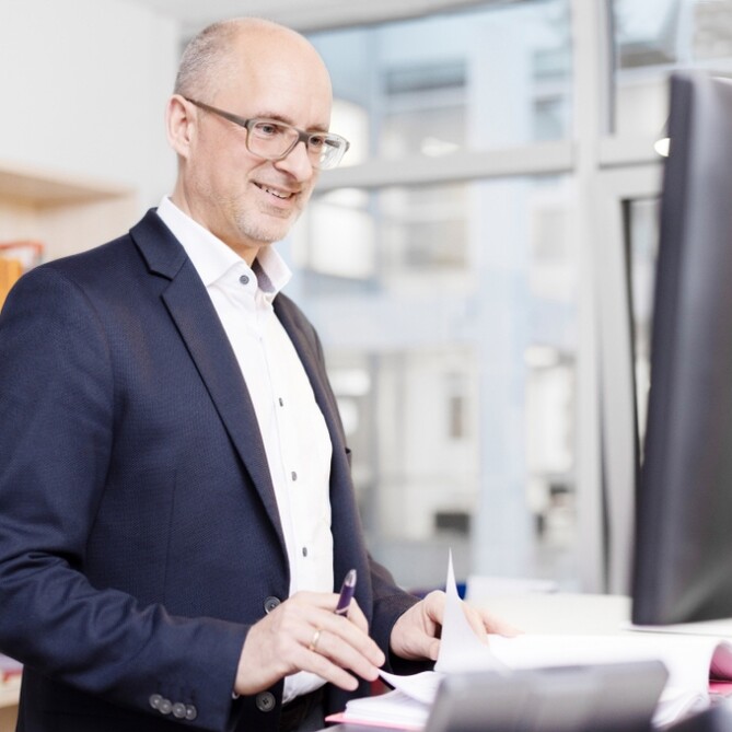 Thomas Bertram steht lächelnd am Schreibtisch